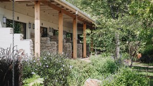 Un espace extérieur abrité, doté de murs en pierre et de poutres en bois, entouré d’une végétation luxuriante et de plantes en fleurs.