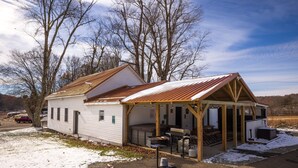 A single-story mobile home with a metal roof, a covered porch, and a barbecue area. - The Grange (In the Heart of the Hocking Hills) (Laurelville)