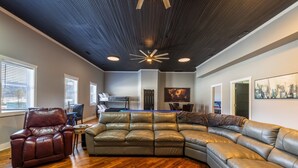A spacious living room with a large L-shaped sectional sofa, a leather armchair, and a wooden floor. - The Grange (In the Heart of the Hocking Hills) (Laurelville)