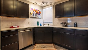 A modern kitchen with dark cabinets, a stainless steel dishwasher, a sink, and a backsplash. - The Grange (In the Heart of the Hocking Hills) (Laurelville)
