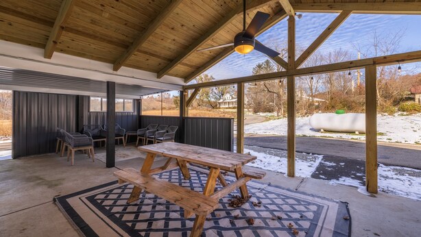 A covered outdoor area with a wooden picnic table, chairs, and a ceiling fan. - The Grange (In the Heart of the Hocking Hills) (Laurelville)