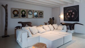 Un salon moderne avec un grand canapé d’angle, une sculpture en bois représentant un arbre et une série d’œuvres d’art encadrées accrochées au mur.