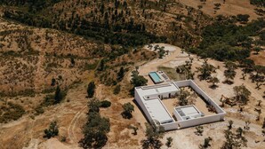 Vue aérienne d’un bâtiment moderne doté d’une piscine, entouré d’un paysage aride et vallonné où la végétation est rare.