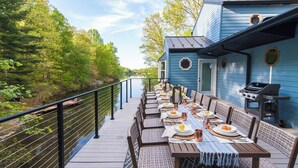A deck with a long table set for dining, overlooking a river.