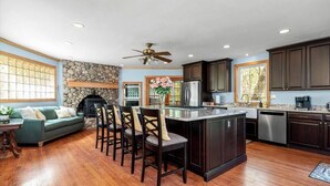 A spacious kitchen with dark wooden cabinets, a central island, and a stone fireplace.