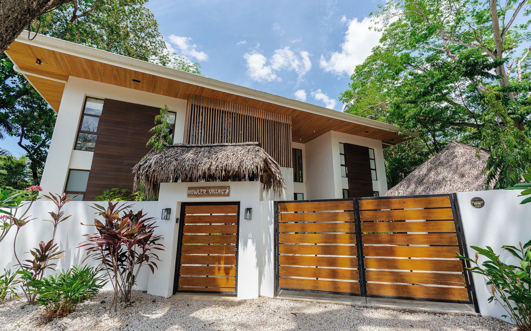A modern villa with a thatched roof entrance, a wooden gate, and a sign reading "HOWLER VILLAS".