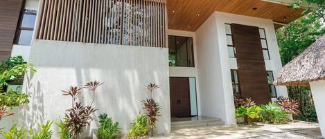 Un edificio moderno con una entrada de listones de madera, un camino de hormigón y varias plantas.