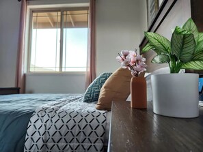 A bedroom with a bed, a bedside table, a window, and a potted plant.