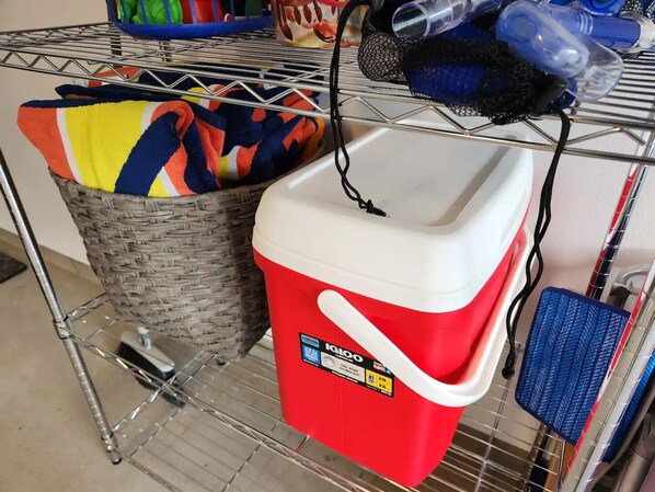 A red cooler with a white lid and a label, a wicker basket, and a metal shelf with various items. - Brand New 4BHK Home! Ocean and Mountain View! (Waianae)
