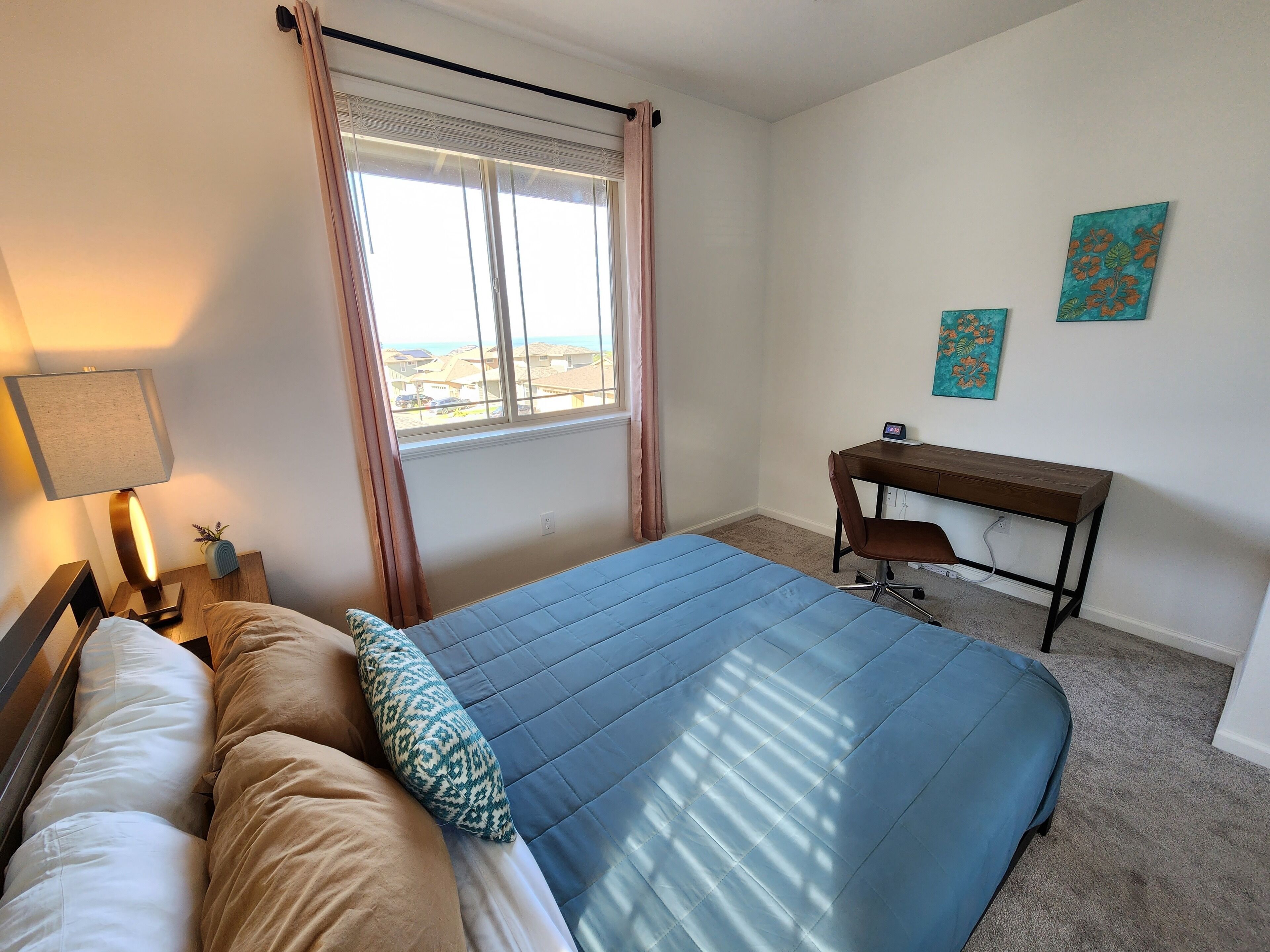 A bedroom with a bed, a desk, a lamp, and a window with curtains.