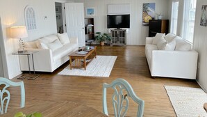 A spacious living room with two white sofas, a wooden coffee table, and a TV stand. - Charming Bayfront Getaway - Private Pier (Fairhope)