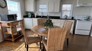A kitchen with white cabinets, a dining table with wicker chairs, a microwave, a coffee maker, and a stove. - Charming Bayfront Getaway - Private Pier (Fairhope)