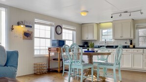 A dining area with a wooden table and chairs, a television, and a kitchen in the background. - Charming Bayfront Getaway - Private Pier (Fairhope)