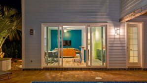A swimming pool with a tiled edge, a sliding glass door leading to a room with a sofa and a television, and a small outdoor seating area with a chair. - Oversized home w/ Heated Pool - mins from beach! (St. Augustine)