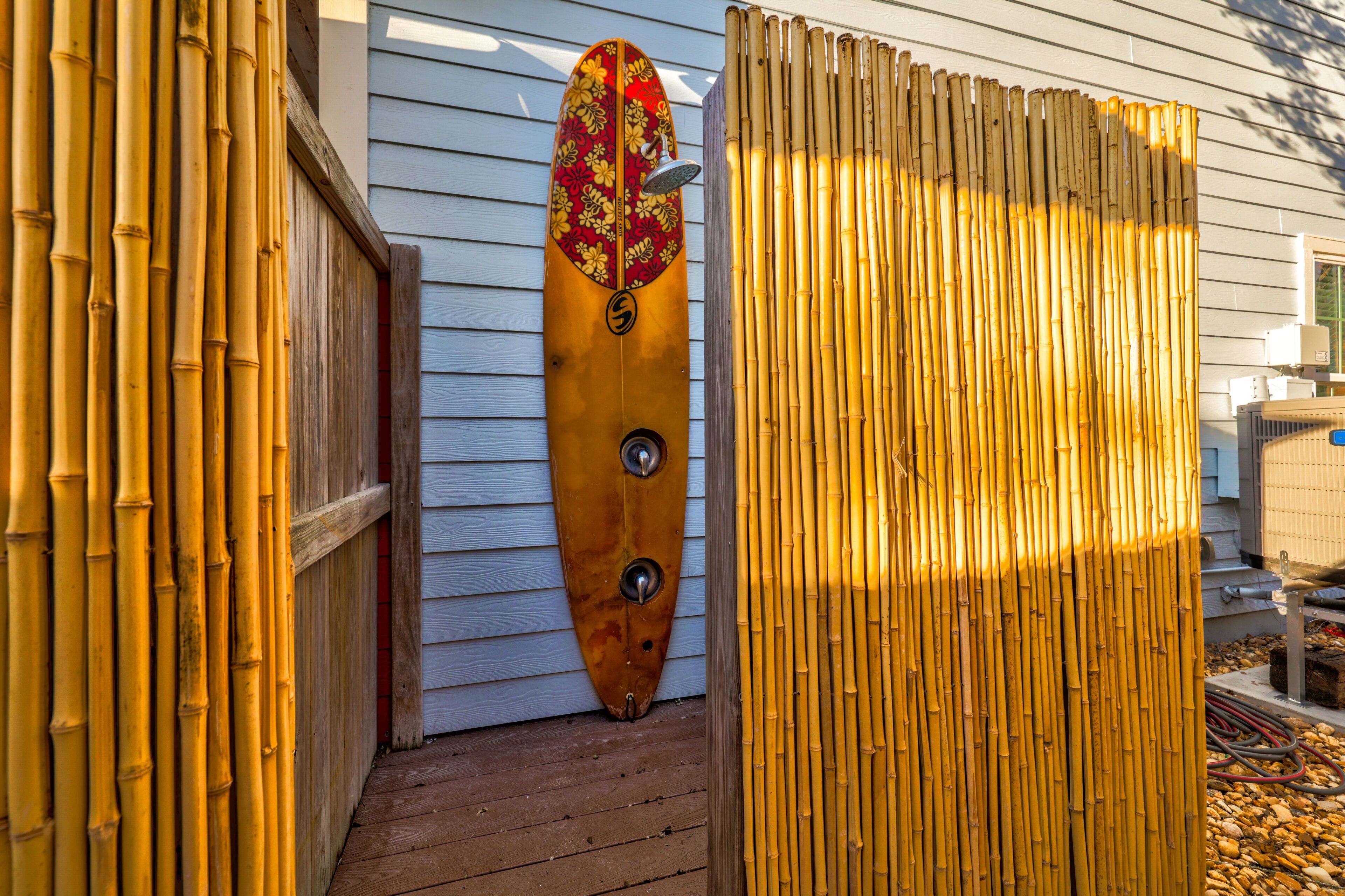 Een houten terras met een surfboard tegen een witte gevel.