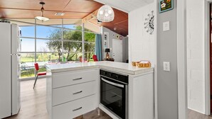 Eine Küche mit weißen Schränken, einem schwarzen Backofen und einem großen Fenster mit Blick ins Freie.