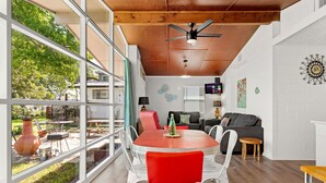Ein Essbereich mit einem Glastisch und roten Stühlen, einem schwarzen Sofa und einem Fernseher im Hintergrund.