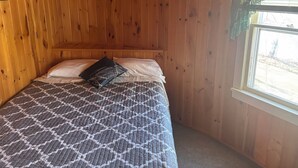 Ein Zimmer mit Holzwänden, einem Bett, einem Fenster mit Aussicht und einem hölzernen Kopfseitenverkleidung.