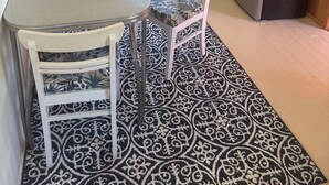 Eine kompakte Küche mit Esstisch, Stühlen, einem gemusterten Teppich, einem Kühlschrank, einer Mikrowelle und einem Fenster mit Vorhang.