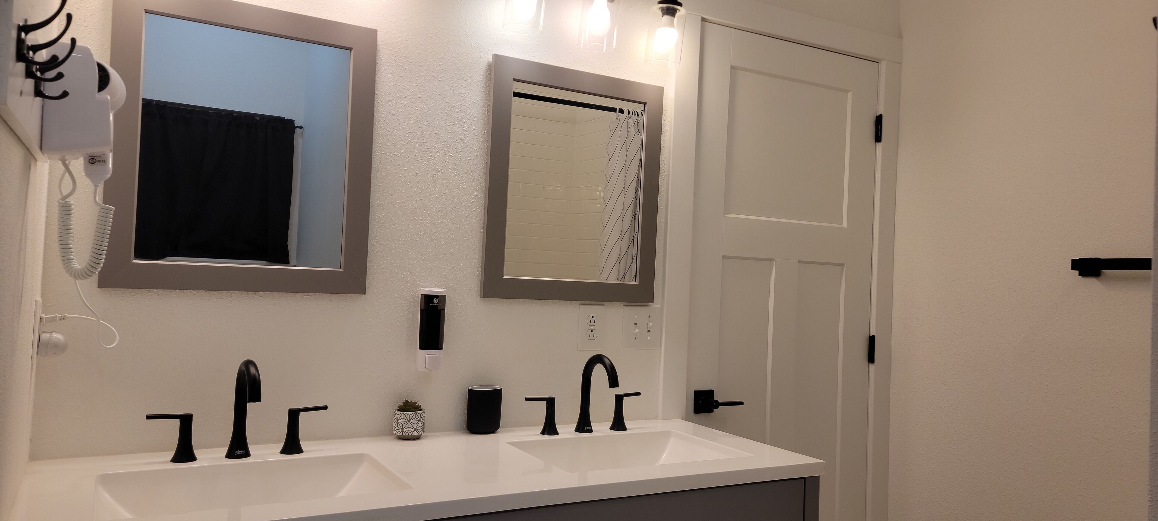 A bathroom with two sinks, a hairdryer, a mirror, and a shower curtain.