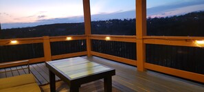 Une terrasse en bois avec une table et des chaises, une rambarde et une vue sur un paysage vallonné.