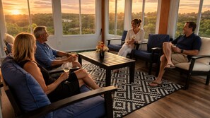 A group of people seated on sofas and chairs in a room with a large window, a coffee table, and a patterned rug. - Modern Luxury 5BR 4BA with Heated Pool and EV Charge (Branson)
