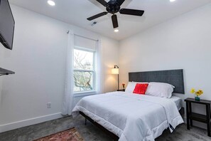 Un dormitorio con cama, ventilador de techo, mesita de noche, lámpara y ventana.