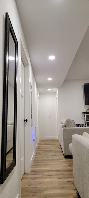A hallway with a wooden floor, white walls, and a gray sofa.