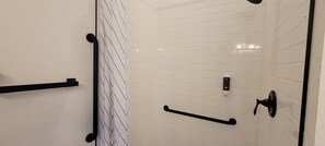 Une salle de bain avec des murs recouverts de carreaux blancs, un porte-serviettes noir, une barre dâappui noire et une poignĂ©e de porte noire.