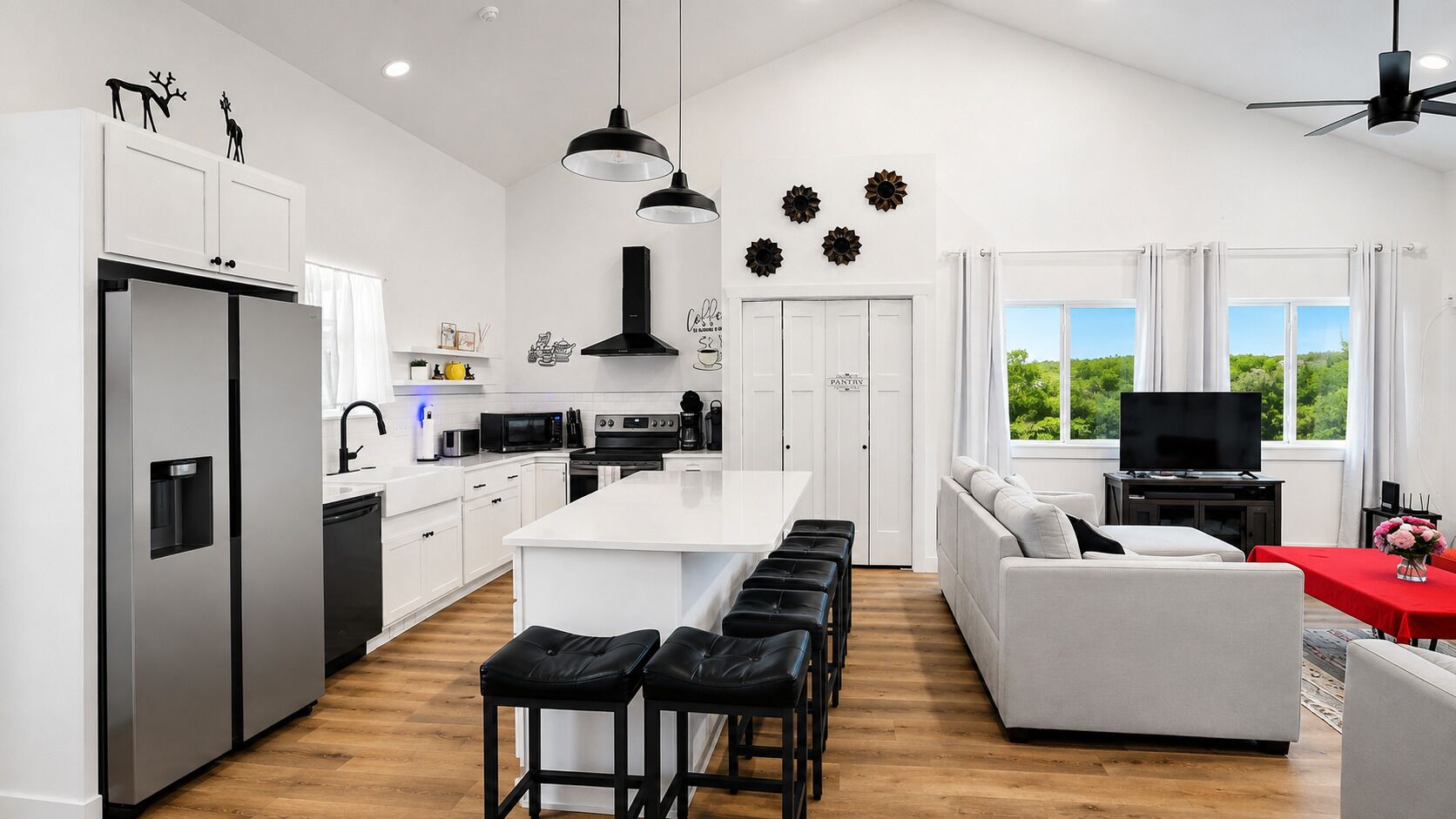 Une cuisine moderne avec un îlot central, un coin repas avec une table rouge et un salon avec un canapé et une télévision.