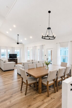 A spacious living room with a large wooden dining table, multiple seating options, and a ceiling fan. - Modern Luxury 5BR 4BA with Heated Pool and EV Charge (Branson)