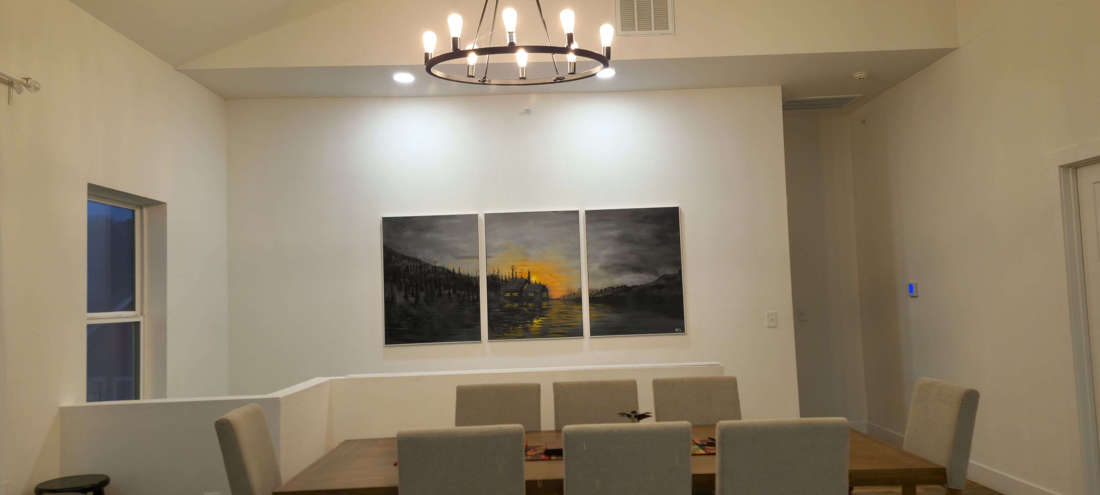 Un comedor con una mesa, sillas y tres cuadros en la pared.
