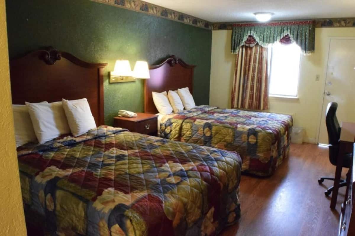 A room with two beds, a desk, a chair, a lamp, and a window with curtains.