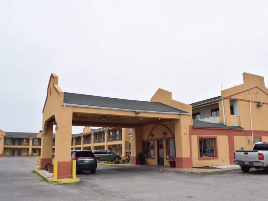 Um motel com área de estacionamento coberta, vários quartos e um pequeno espaço comercial.
