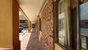A corridor with a brick wall, a covered walkway, and a view of parked cars. - Deluxe Inn By Capital O Odessa I-20 (Odessa)