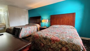 A hotel room with two beds, a desk, a chair, and a nightstand with a lamp. - Deluxe Inn By Capital O Odessa I-20 (Odessa)