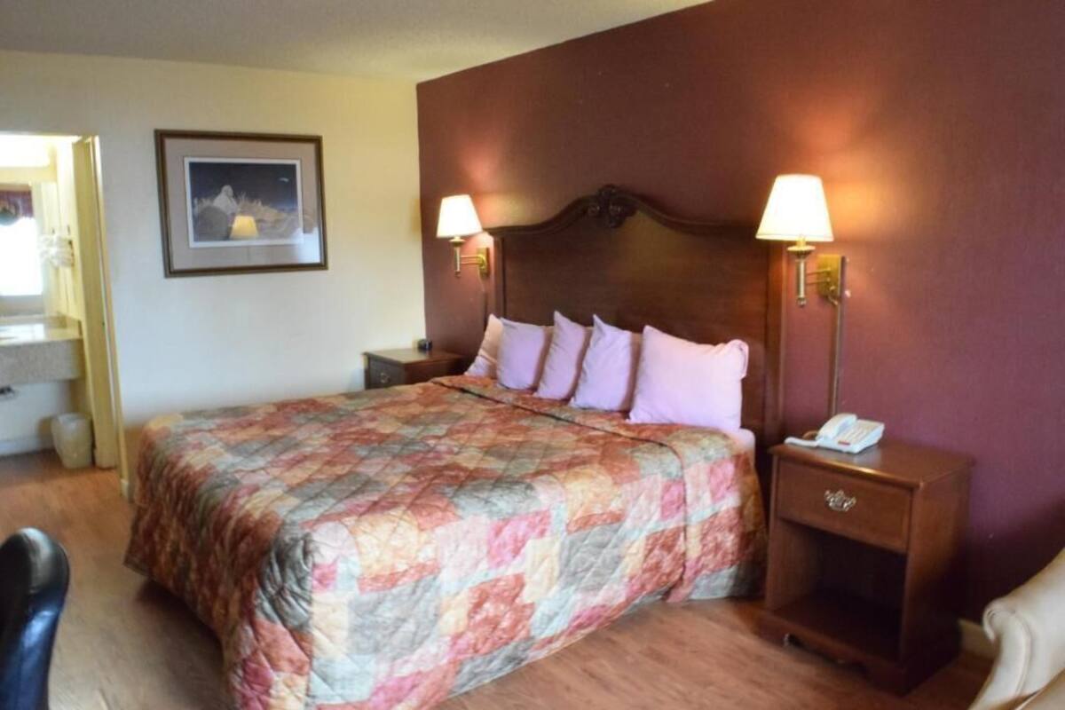 A hotel room with a large bed, two bedside lamps, a nightstand with a phone, and a framed picture on the wall.