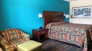 A hotel room with a bed, a chair, a nightstand, and a small table. - Deluxe Inn By Capital O Odessa I-20 (Odessa)