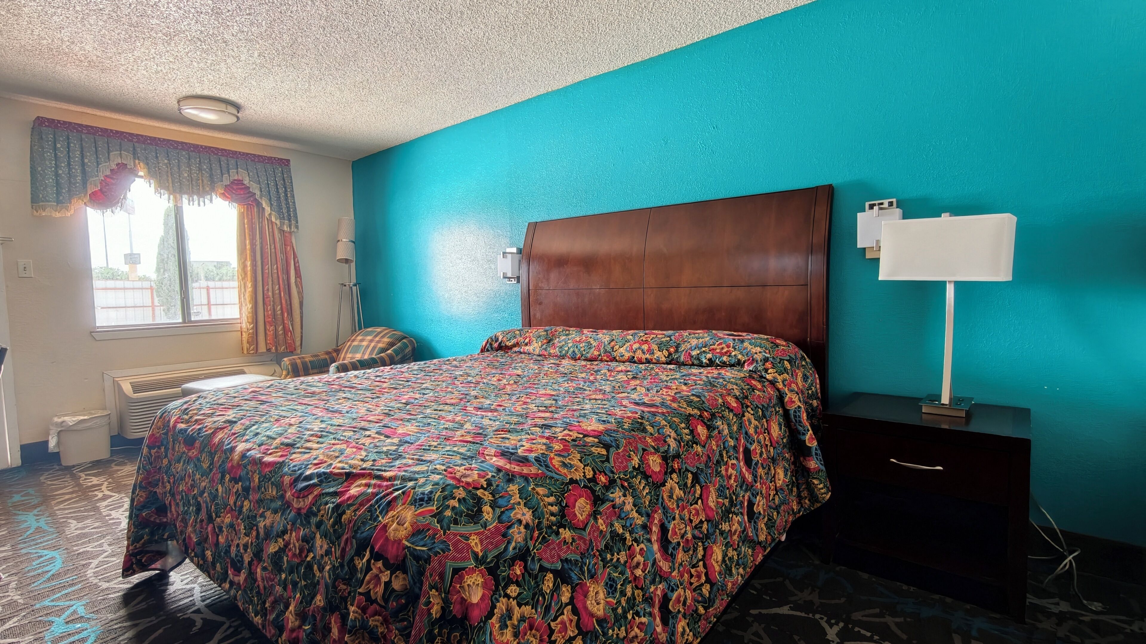 A hotel room with a large bed, a nightstand, a lamp, and a window with curtains.