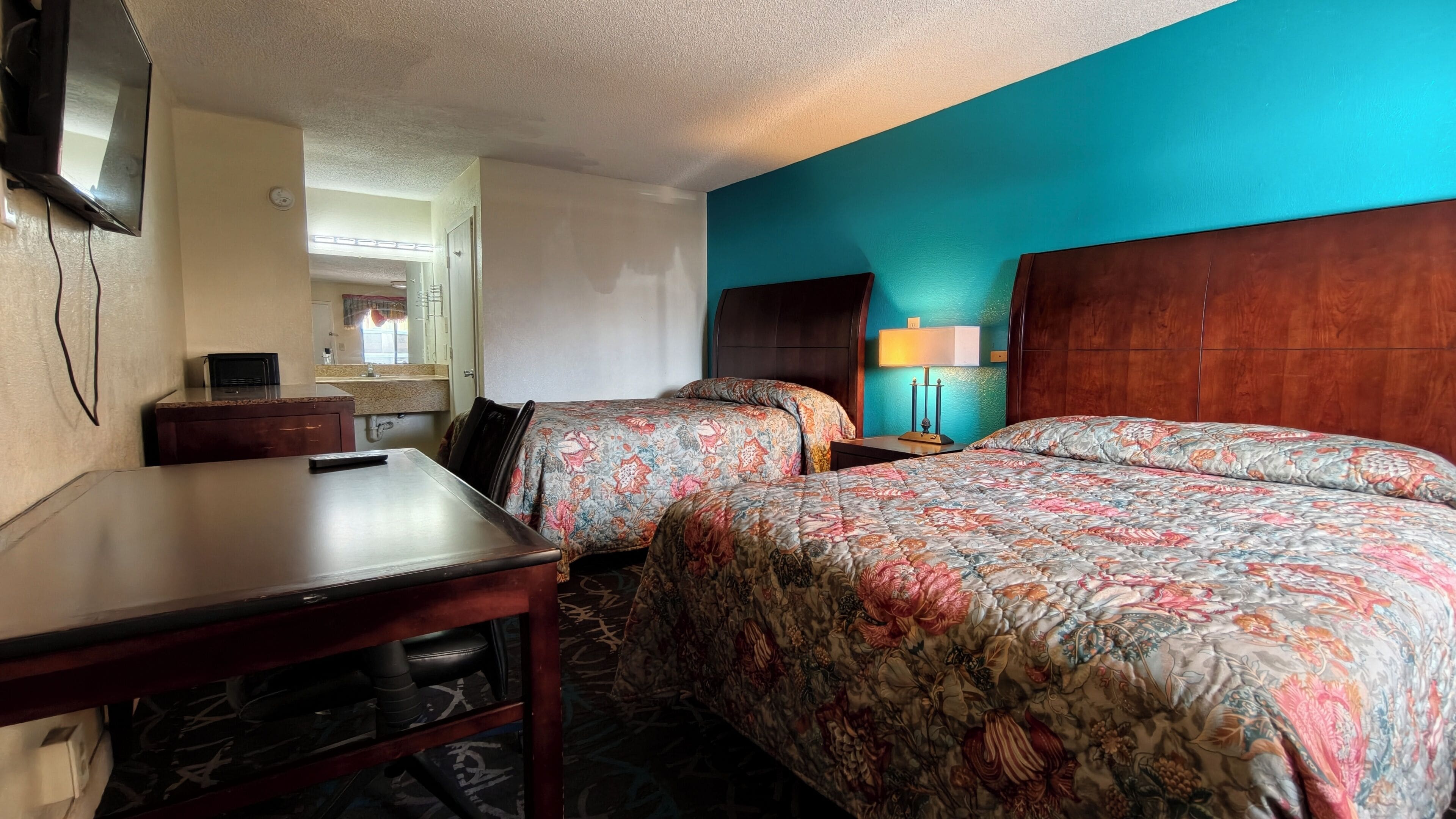 A hotel room with two beds, a desk, a TV, and a bathroom visible through an open door.
