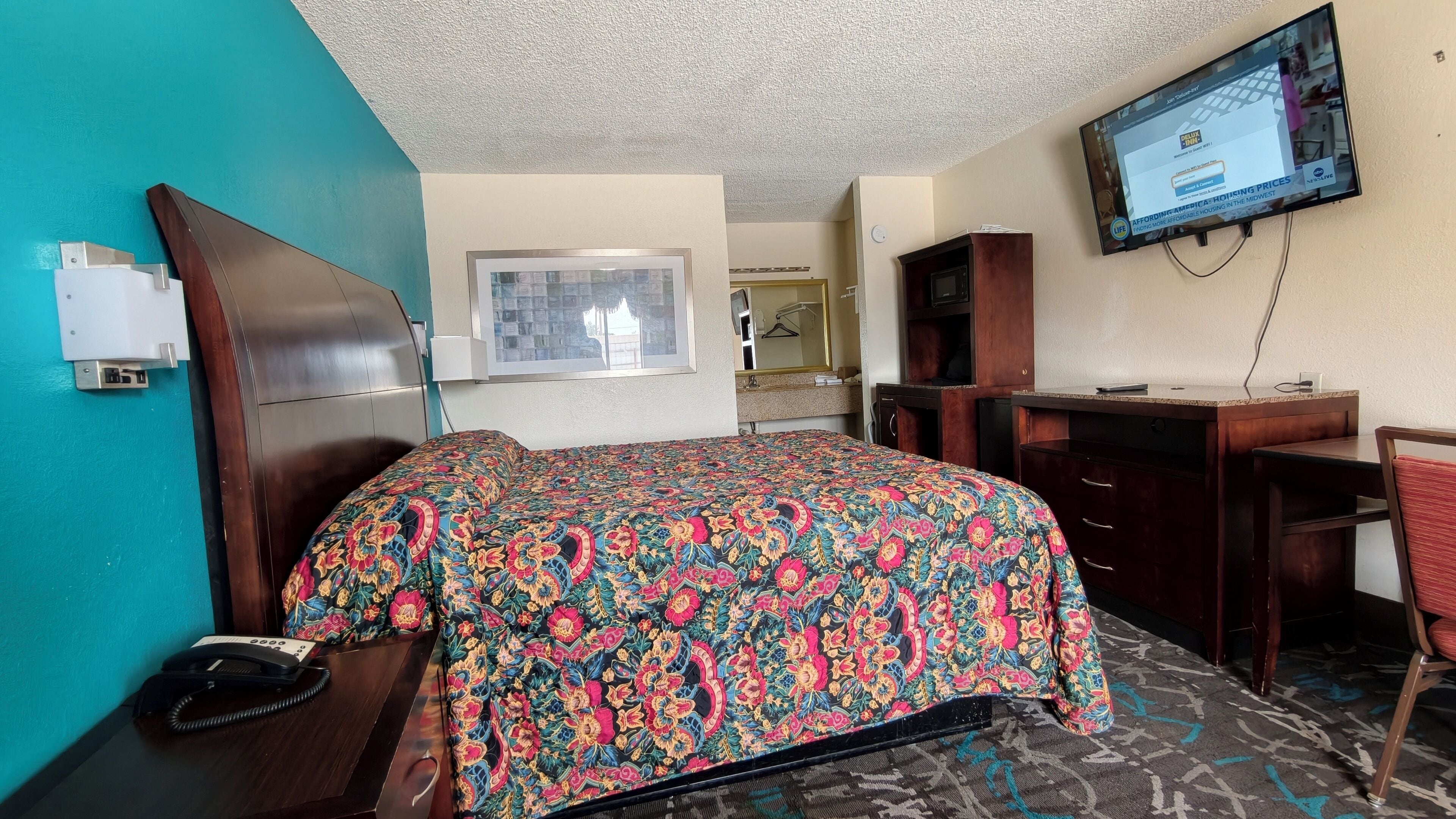 A hotel room with a bed, desk, chair, television, and a telephone.