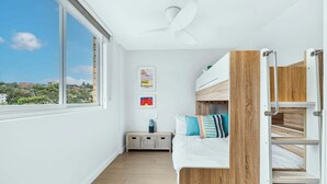Un dormitorio moderno con literas, una mesita de noche pequeña y vistas a la ciudad a través de un ventanal grande.