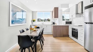 Una cocina moderna con armarios blancos, un refrigerador de acero inoxidable y una zona de comedor con mesa de madera y sillas negras.