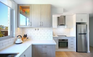 A modern kitchen with white cabinetry, a stainless steel refrigerator, and a window with a view.