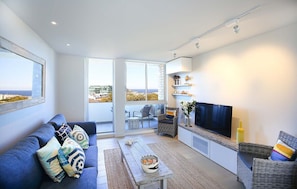 A modern living room with a sofa, a coffee table, a TV, and a balcony with a view.