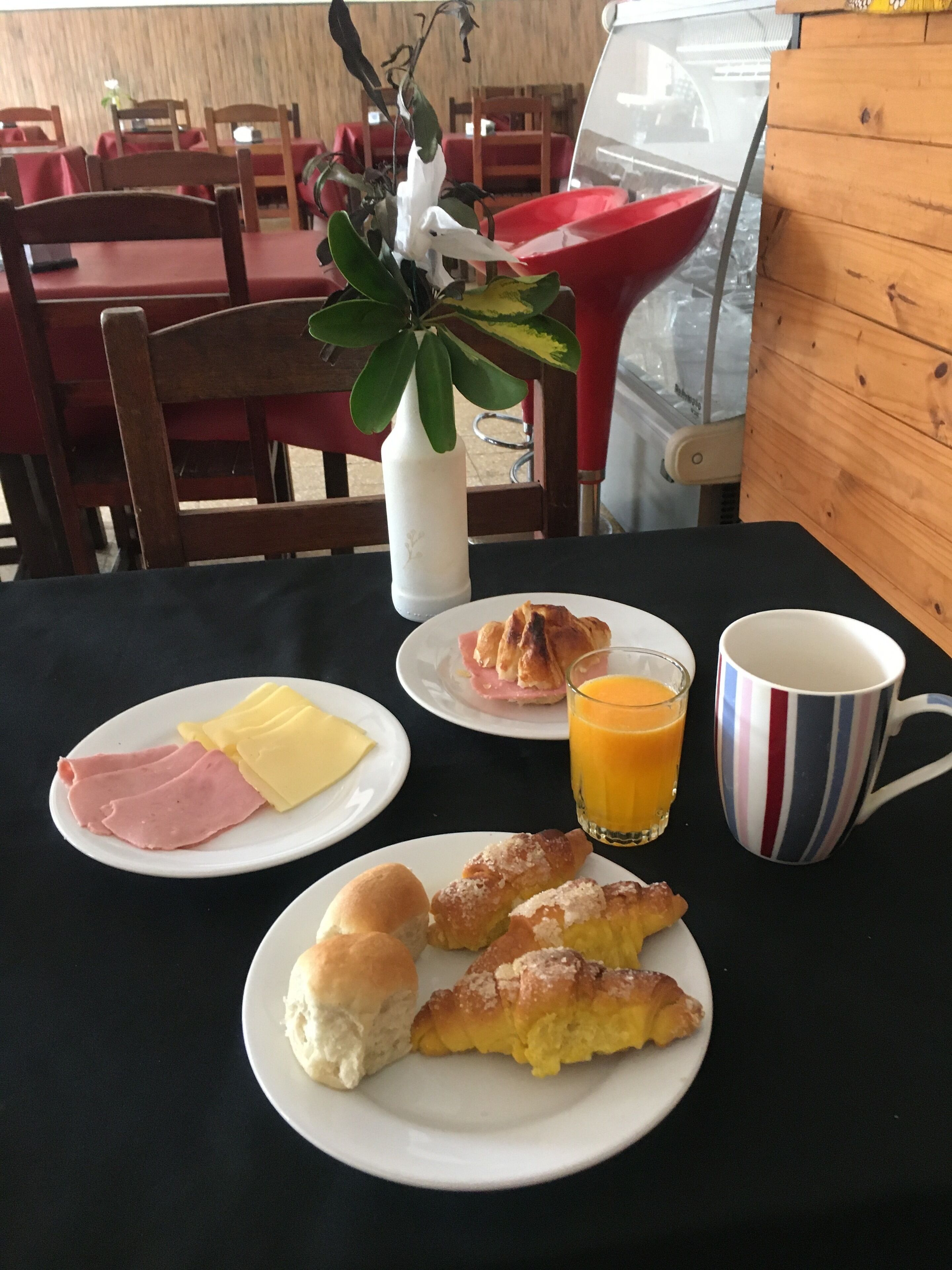A breakfast setting with plates of ham, cheese, croissants, and a glass of orange juice.
