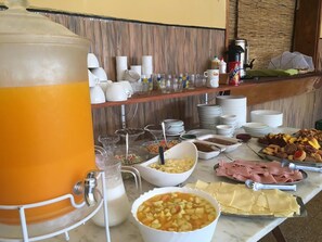 Un bufé con diversos alimentos, entre ellos frutas, verduras y carnes, además de una jarra grande de jugo de naranja.