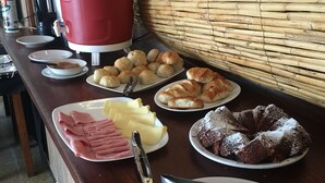 A buffet table with various food items including pastries, ham, and a cake. - Hotel Alcázar  (Piriapolis)