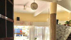 A spacious living area with a staircase, a chandelier, and a view of the street outside. - Hotel Alcázar  (Piriapolis)