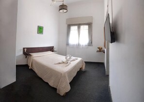 Un dormitorio con cama, una ventana pequeña, televisor montado en la pared y ventilador de techo.